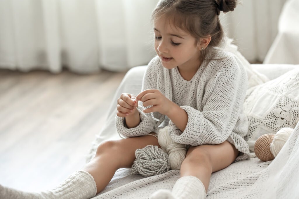 enfant cute little girl with threads learns to knit.