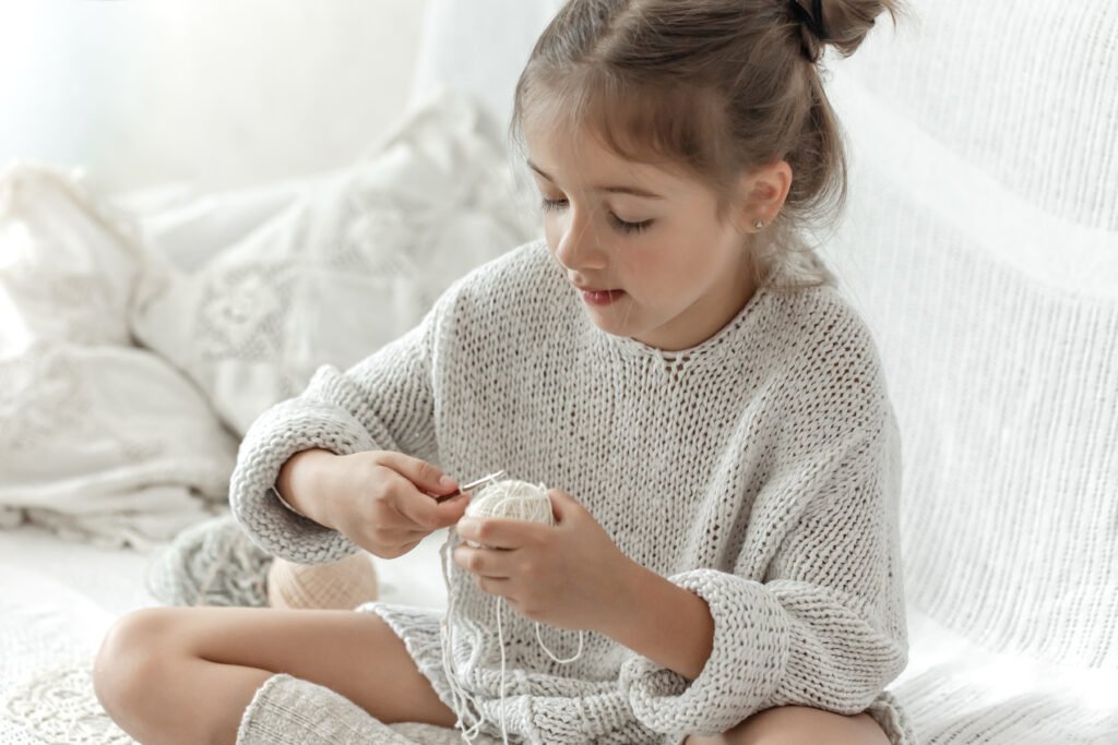 enfant cute little girl with a ball of thread learns to knit.